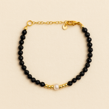 Bracelet with black beads, gold chain, and pearl on a beige background      